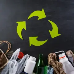 Zielony symbol recyklingu nad różnymi odpadami: papier, plastik, szkło.