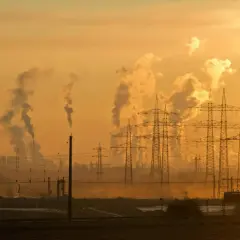 Dymiące kominy fabryk i linie energetyczne na tle zachodzącego słońca. To obraz przemysłowego krajobrazu, który ilustruje przyczyny zmian klimatu.