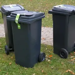Trzy szare kosze na śmieci stoją na trawie. Zastanawiasz się, gdzie wyrzucić kołdrę z pierza? Sprawdź lokalne przepisy dotyczące odpadów wielkogabarytowych.