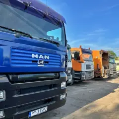 Rząd ciężarówek, w tym śmieciarek, gotowych do odbioru materiałów z recyklingu.