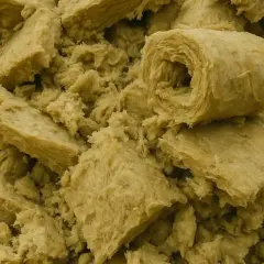 Góra pokruszonej wełny mineralnej, gotowa do utylizacji. Materiał izolacyjny w rolkach i kawałkach.