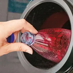 Ręka wkłada czerwoną butelkę do automatu, by odzyskać kaucja za puszki i inne opakowania.