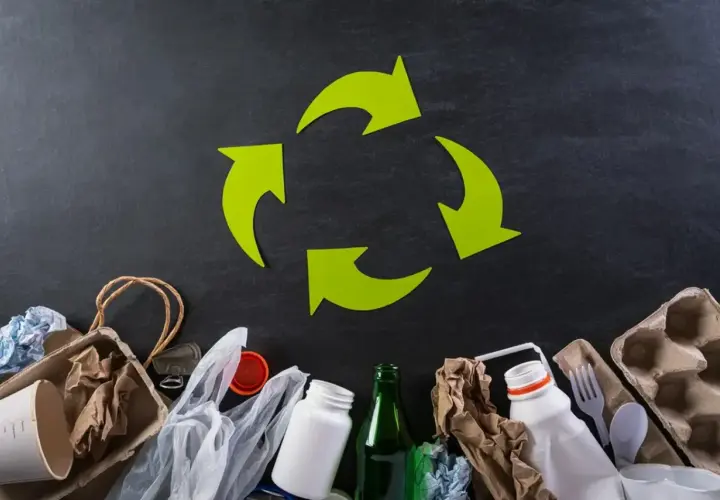 Zielony symbol recyklingu nad różnymi odpadami: papier, plastik, szkło.