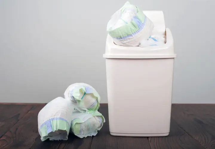 Kupa zużytych pieluch obok kosza, który jest odpowiedzią na pytanie, gdzie wyrzucać pieluchy.