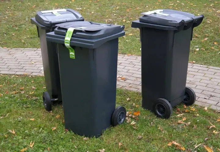 Trzy szare kosze na śmieci stoją na trawie. Zastanawiasz się, gdzie wyrzucić kołdrę z pierza? Sprawdź lokalne przepisy dotyczące odpadów wielkogabarytowych.