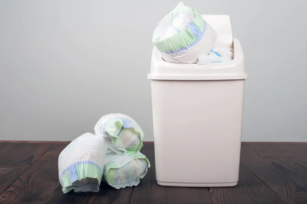 Kupa zużytych pieluch obok kosza, który jest odpowiedzią na pytanie, gdzie wyrzucać pieluchy.