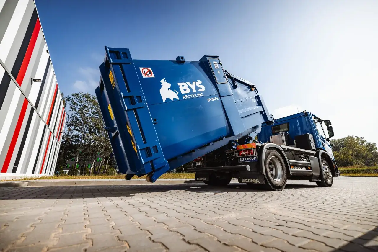 Niebieska śmieciarka z logo BYŚ RECYKLING podczas segregacji odpadów budowlanych.