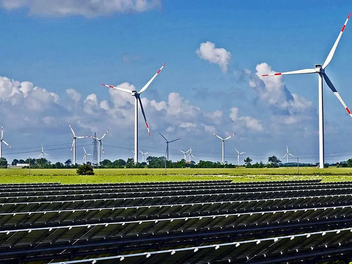 Panele słoneczne i wiatraki na zielonym polu pod błękitnym niebem. To obraz branży OZE, czyli odnawialnych źródeł energii.