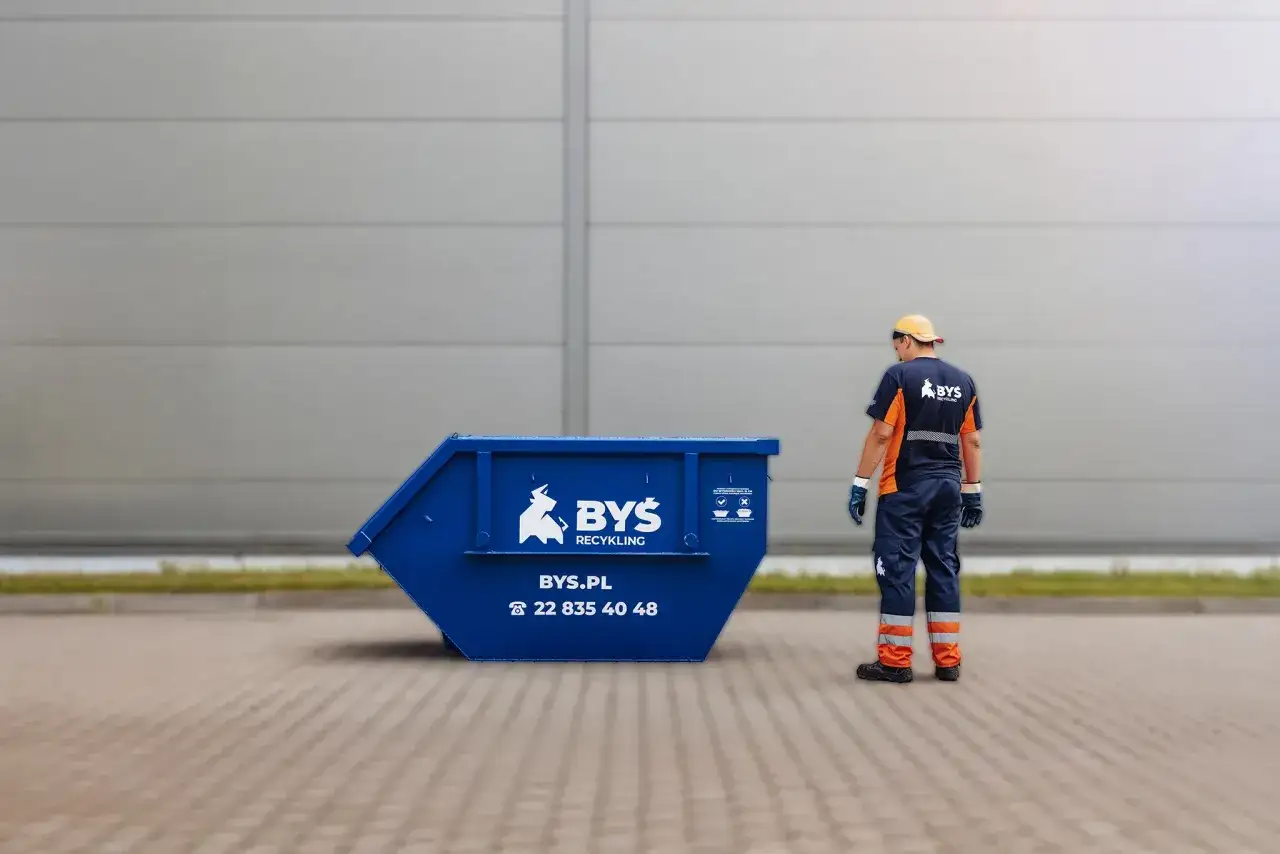 Pracownik firmy BYŚ Recycling stoi obok niebieskiego kontenera. Masz problem, gdzie wyrzucić papę? Zadzwoń!